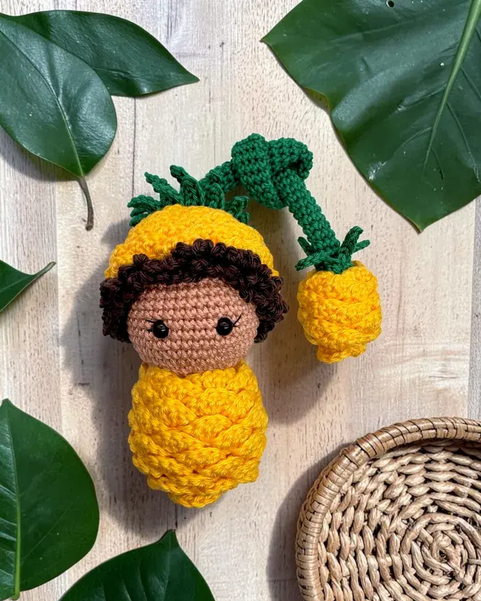 Poupée ananas des Croch’fruits sous une feuille tropicale